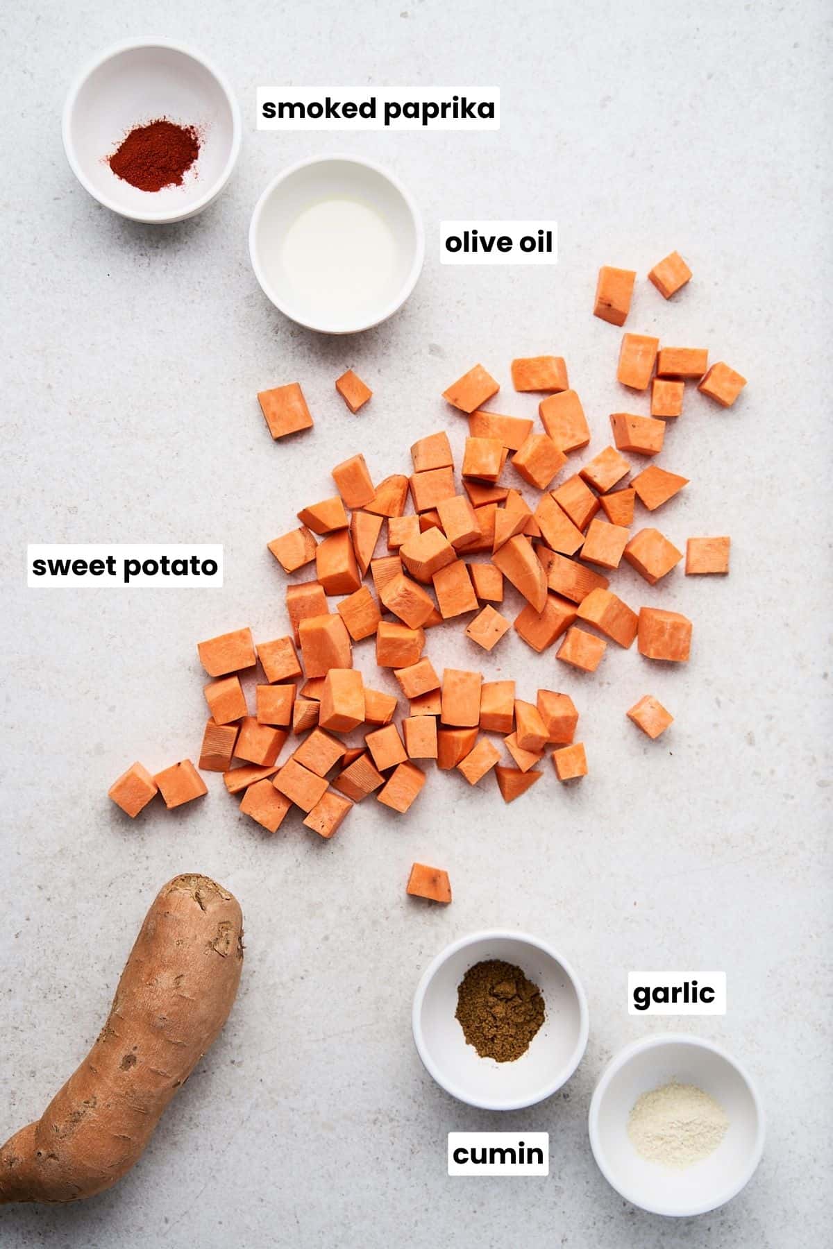 Sweet potato, olive oil, smoked paprika, cum, and garlic on a countertop.