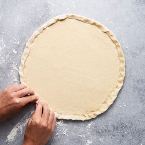 Uncooked pizza dough with crust getting pinched.