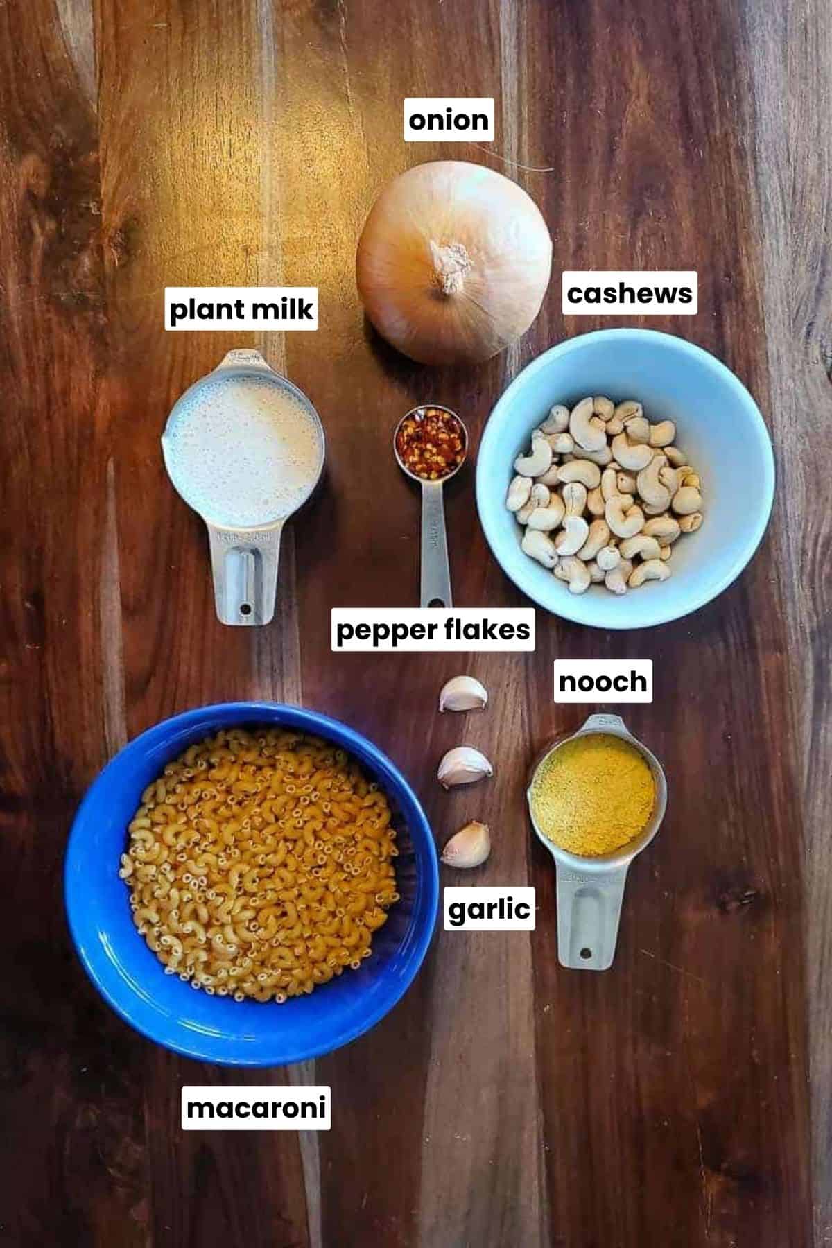 Onion, cashews, pepper flakes, nooch, garlic, and macaroni on a table.