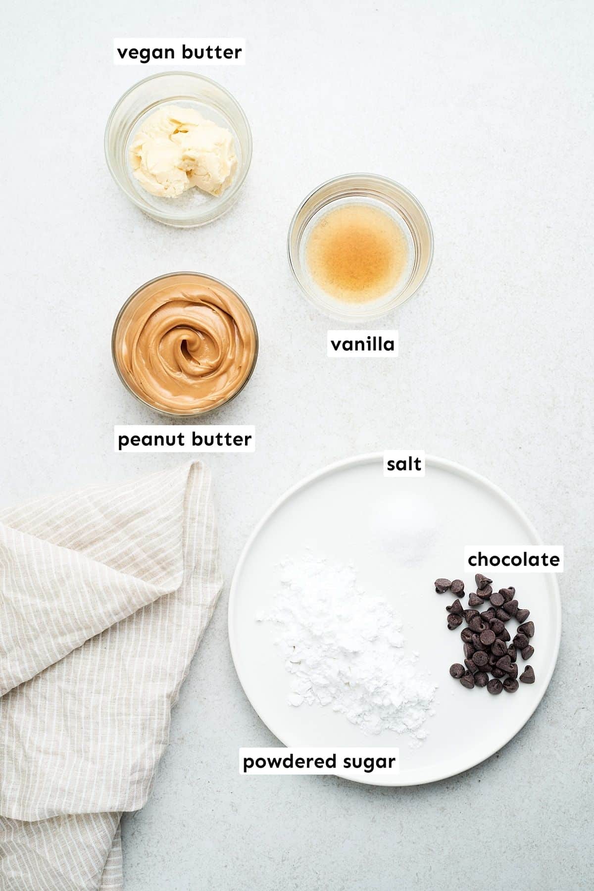 Peanut butter, vegan butter, vanilla, salt, powdered sugar, and chocolate on a table.