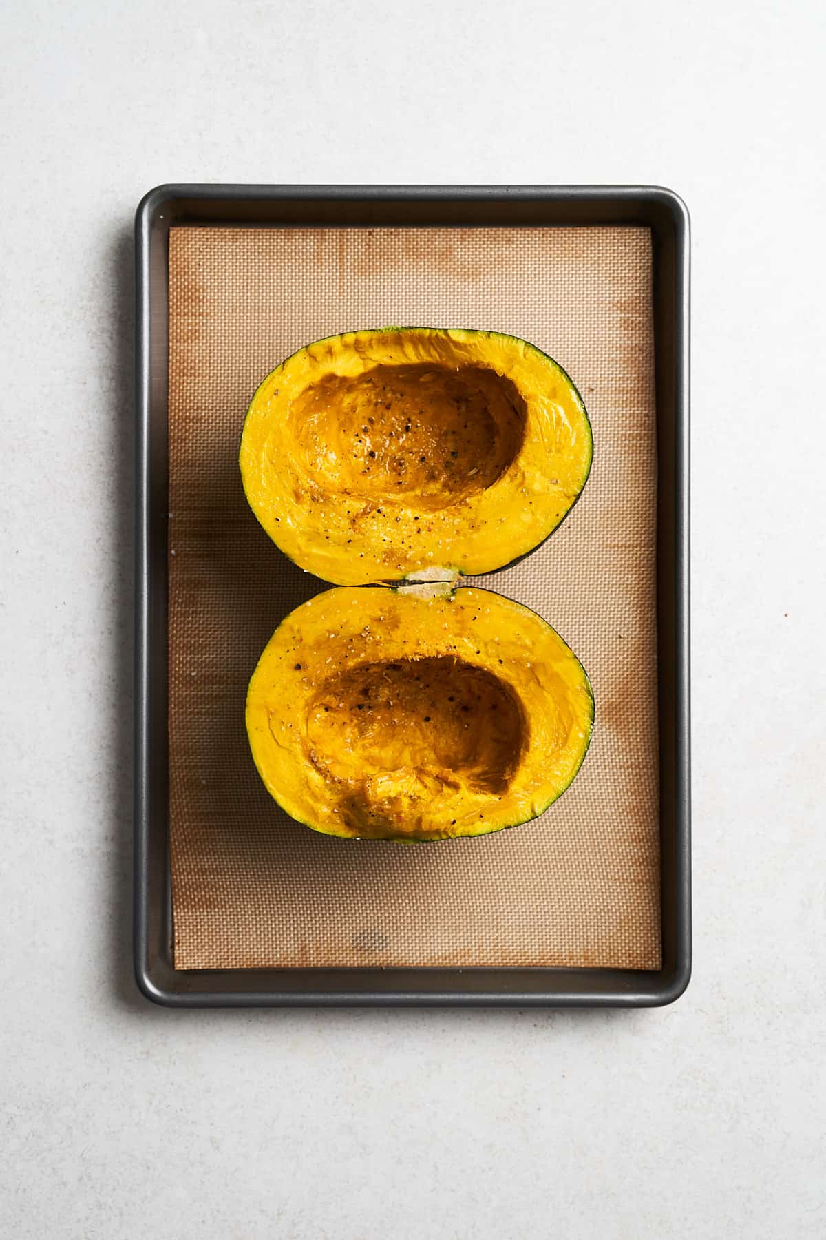 Seasoned kabocha squash halves on a pan.