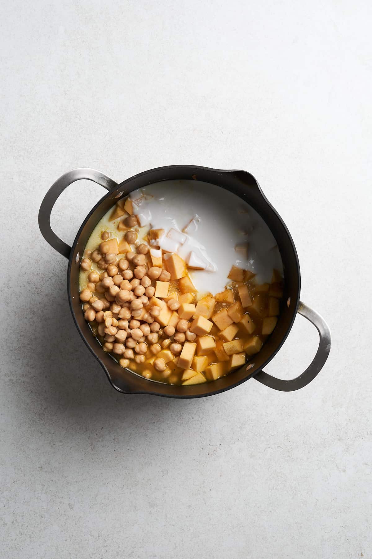 Butternut squash, chickpeas, coconut milk, and broth in a saucepan.