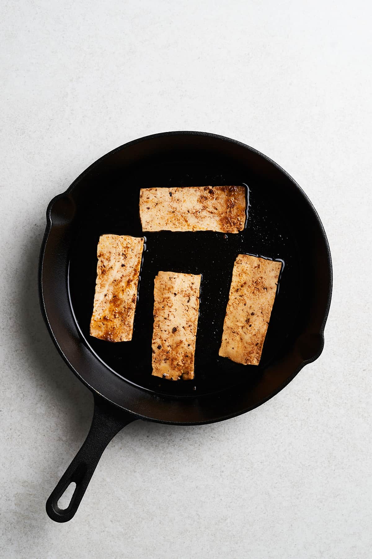 Uncooked tofu strips with seasonings in a frying pan.