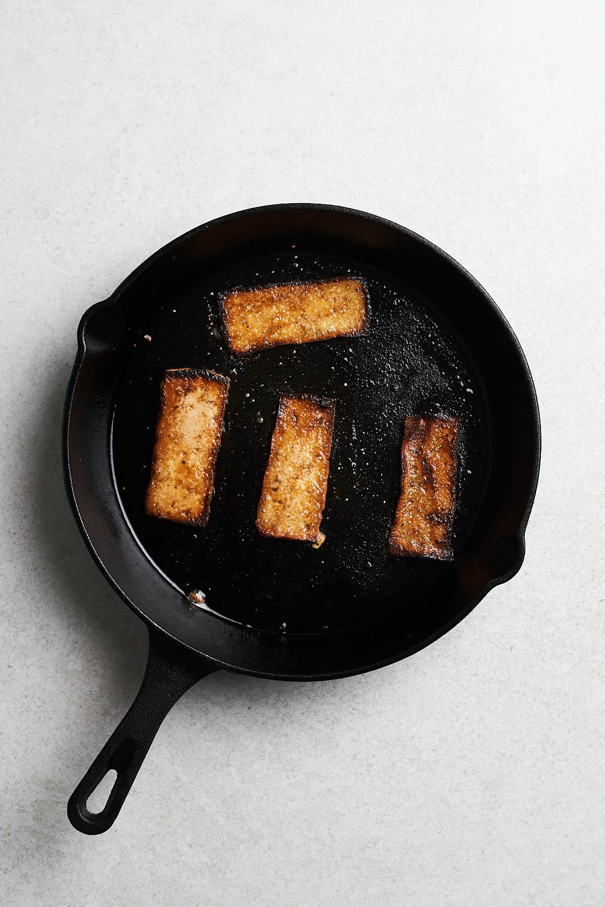 Cooked tofu strips with seasonings in a frying pan.