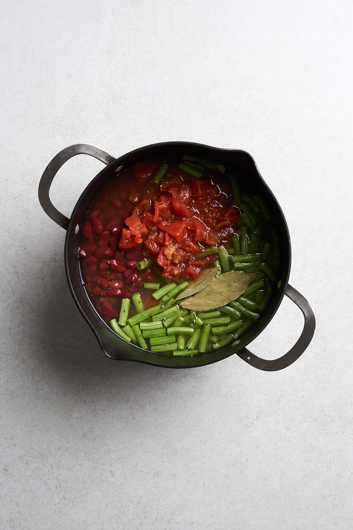 Green beans and tomatoes with vegetable broth in a pot.