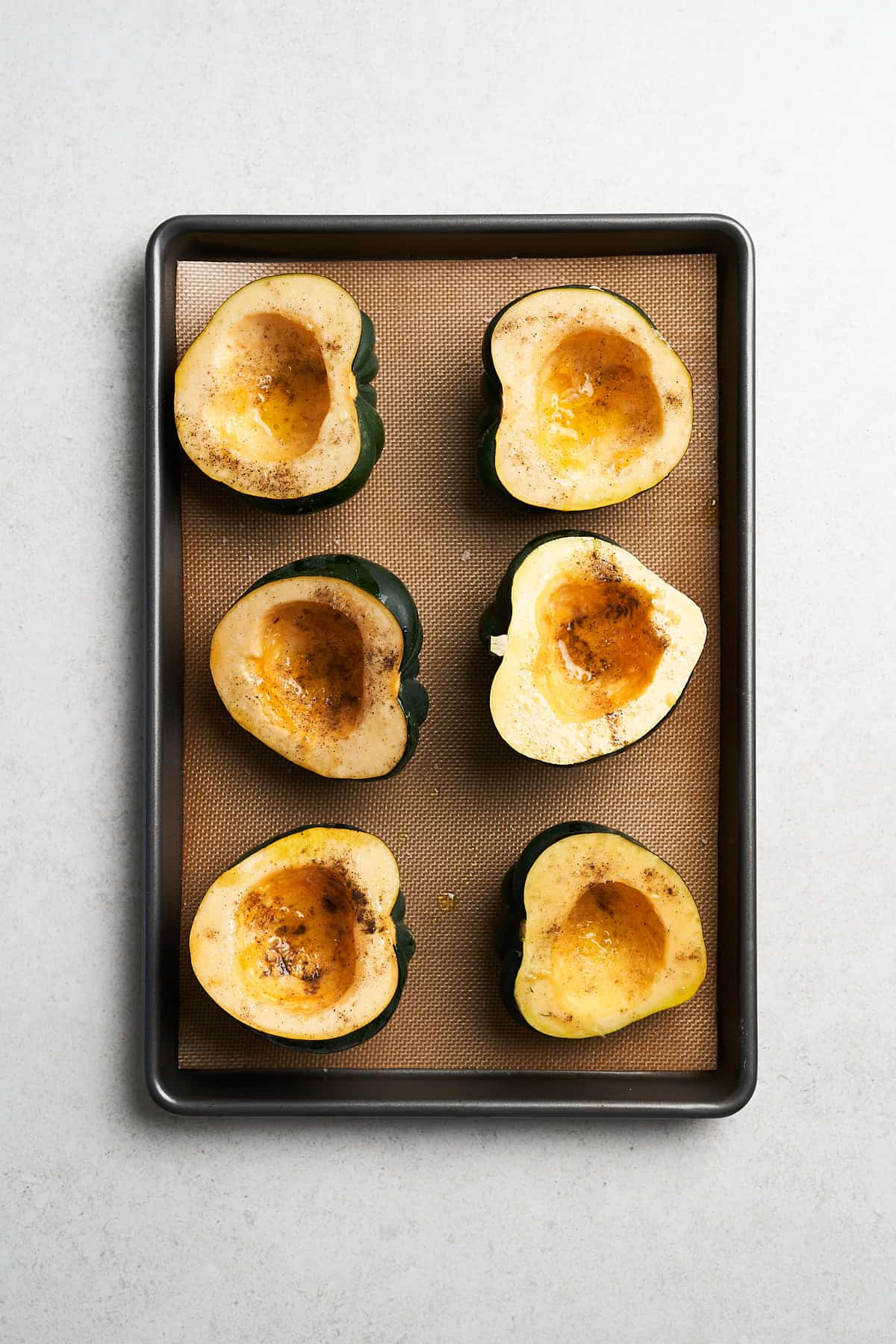 Unbaked acorn squash in a baking pan.