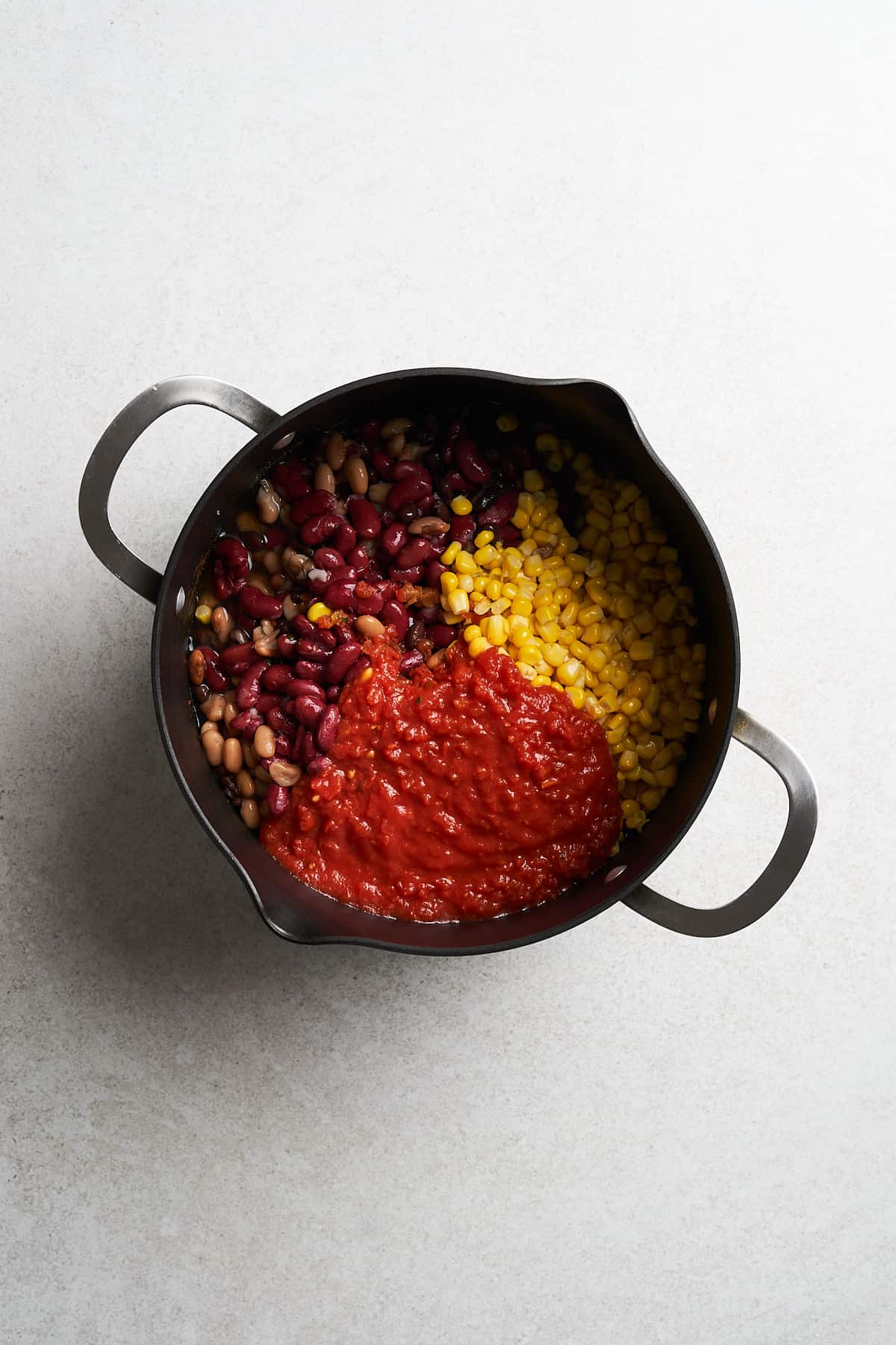 Corn, crushed tomatoes, and other ingredients in a saucepan.